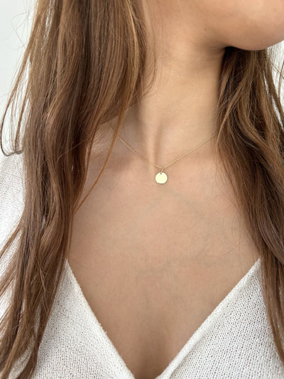 Ronde 14 karaat gouden hanger aan een gouden ketting gedragen door jonge vrouw met bruin haar, decolleté wit shirt 